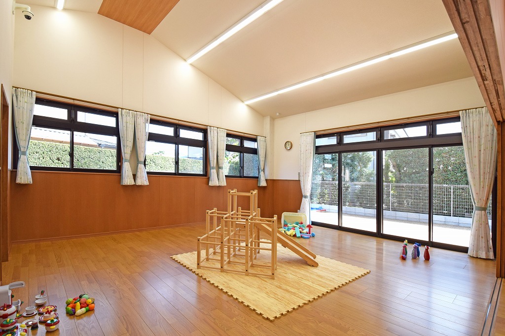 にこにこ保育園の保育室竣工写真。勾配屋根を活かした開放的な高天井と、家庭的な温もりを感じるミディアムブラウンを基調とした落ち着いた内装デザイン