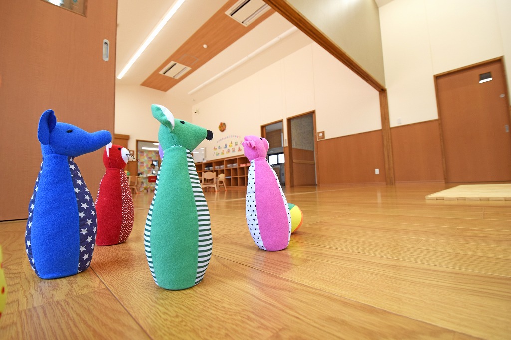 にこにこ保育園の保育室竣工写真。勾配屋根を活かした開放的な高天井と、家庭的な温もりを感じるミディアムブラウンを基調とした落ち着いた内装デザイン