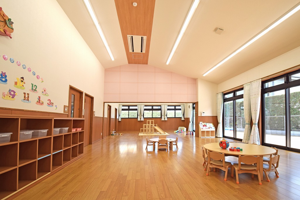 にこにこ保育園の保育室竣工写真。勾配屋根を活かした開放的な高天井と、家庭的な温もりを感じるミディアムブラウンを基調とした落ち着いた内装デザイン