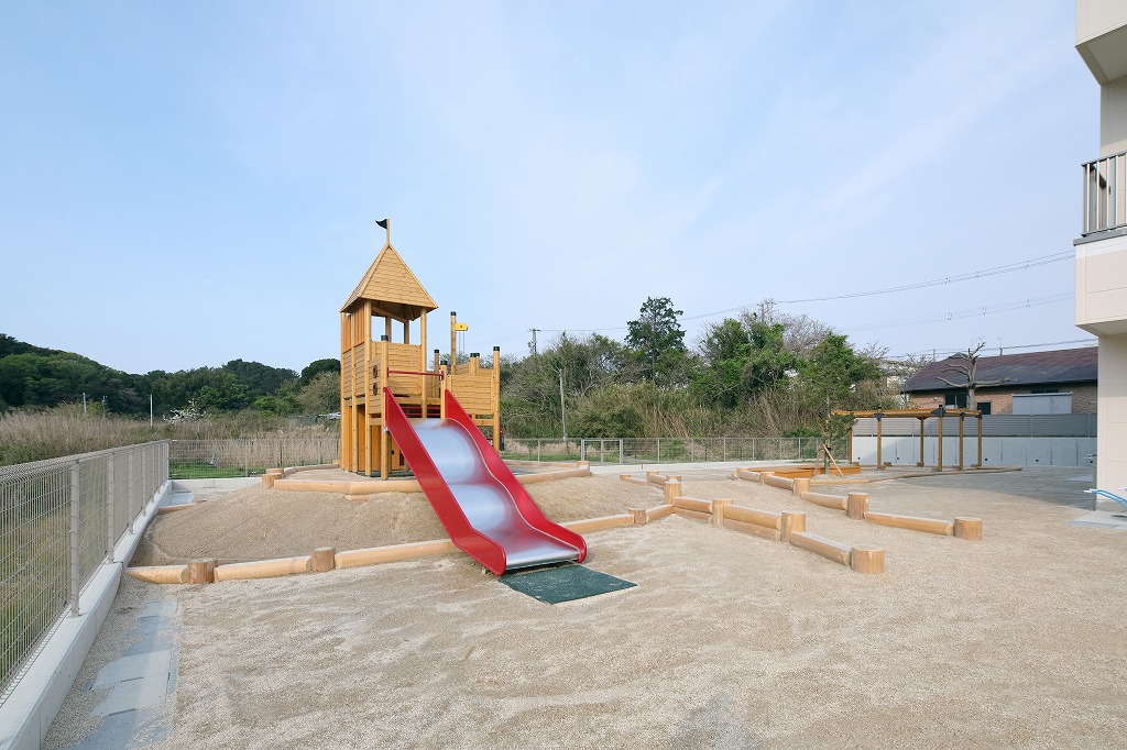 広々とした砂地の園庭に設置された、滑り台が付いたおしゃれな大型木製複合遊具。